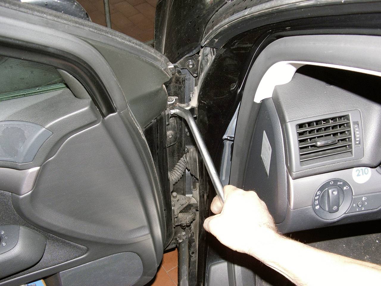 Eine Hand hält einen Schraubenschlüssel, der an der Scharnierstelle einer Autotür angesetzt ist.