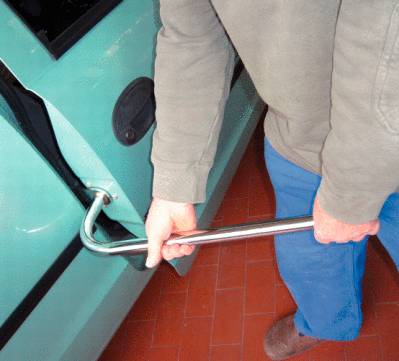 Ein Mann verwendet ein Brecheisen, um die Tür eines Autos zu öffnen. Das Auto hat eine grüne Farbe.