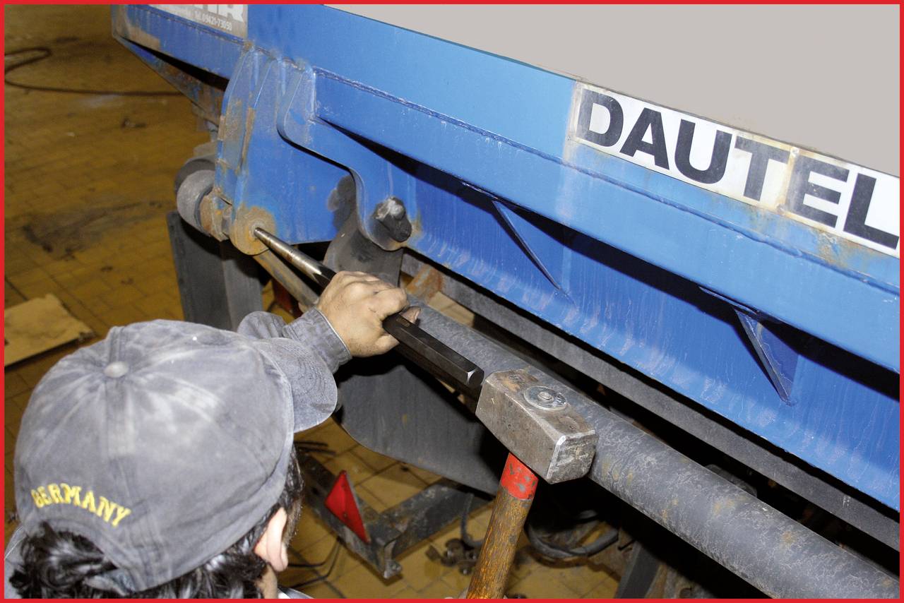 Person mit Mütze benutzt Werkzeug zur Reparatur oder Justierung eines blauen Lastwagenaufbaus. Das Wort 'DAUTEL' ist sichtbar.