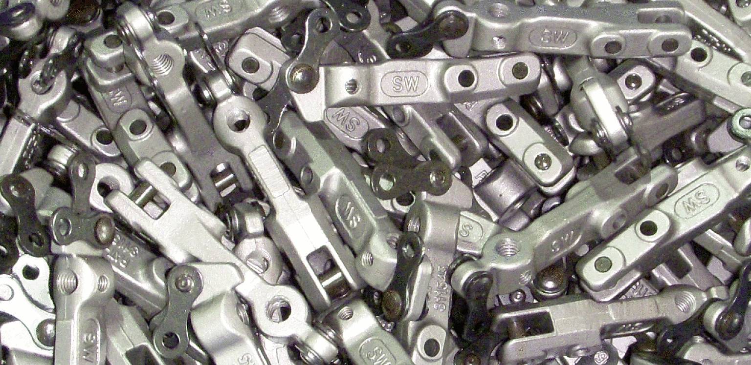 Ein Stapel von Metallbauteilen mit Bolzen und Gravuren, die überwiegend silbern und grau sind. Die Teile scheinen identisch oder ähnlich zu sein.