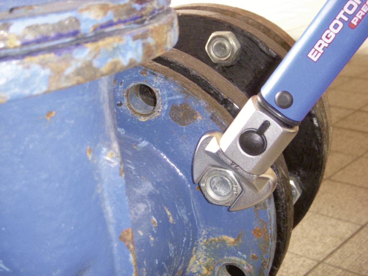 Schraubenschlüssel zieht fest an einer großen Schraube einer rostigen, blauen Metallvorrichtung in einer Werkstatt.