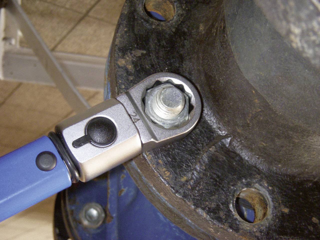 Ein blauer Drehmomentschlüssel zieht eine Schraube an einem Metallflansch fest.