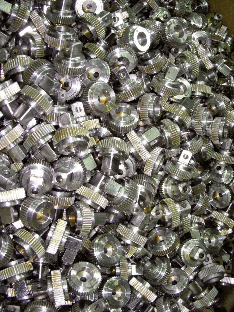 Viele kleine Metallzahnräder in einer Kiste, dicht aneinander gestapelt. Sie zeigen unterschiedliche Formen und Glanzlichter.