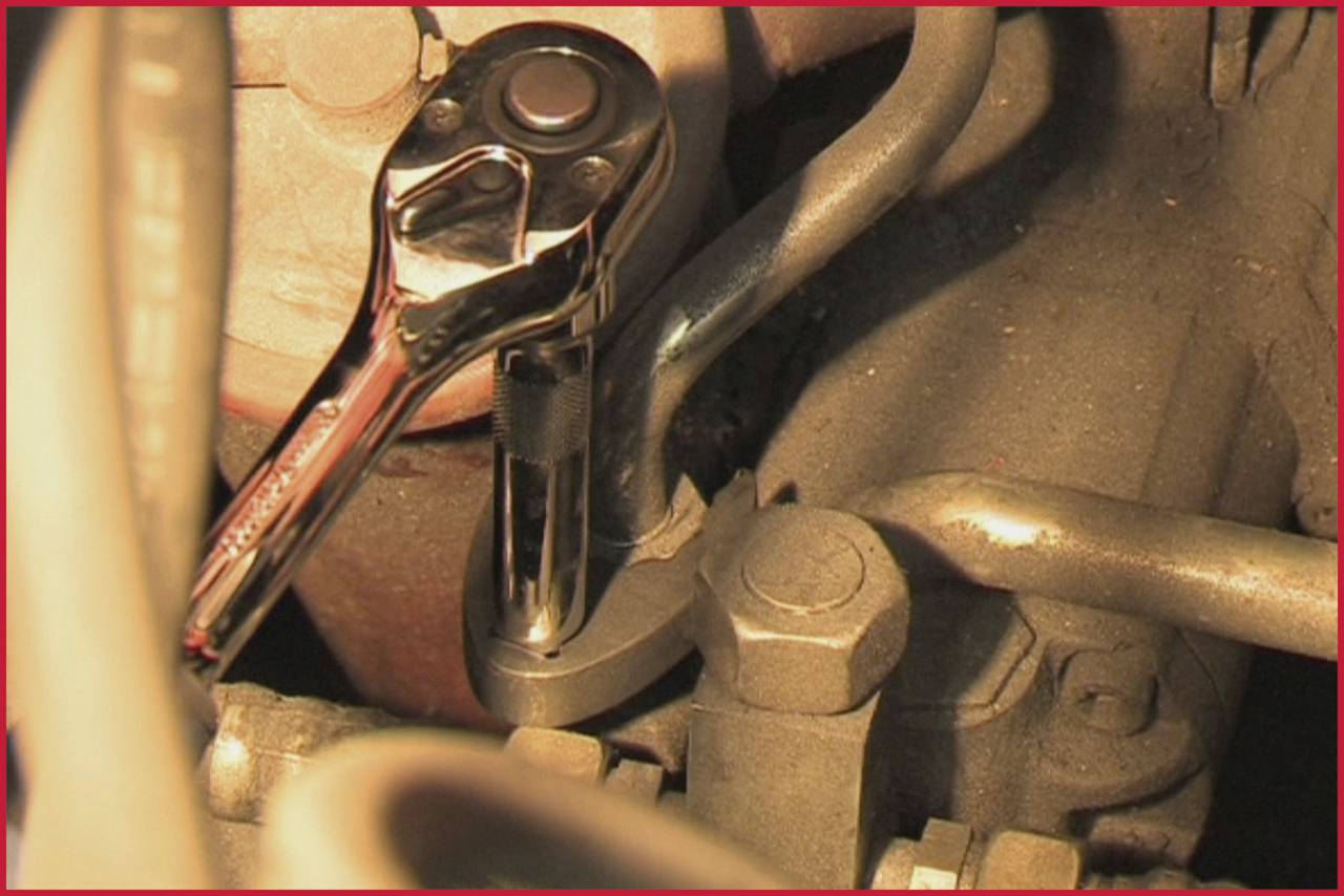 Nahaufnahme eines Ratschenwerkzeugs, das an einer Schraube an einem Motor arbeitet, umgeben von verschiedenen Schläuchen und Metallteilen.
