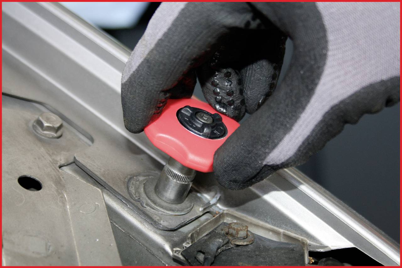 Eine behandschuhte Hand verwendet ein rotes Werkzeug, um eine Mutter an einer Metalloberfläche festzuziehen.