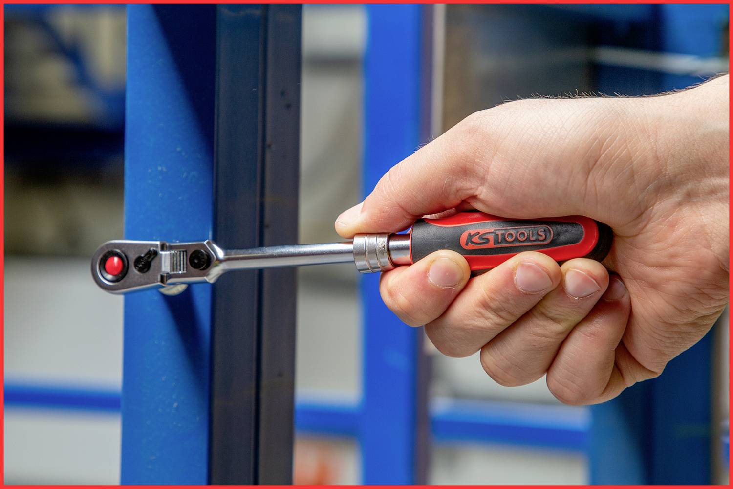 Eine Hand hält einen Ratschen-Schraubenschlüssel, der an einer blauen Metallstruktur arbeitet. Der Schraubenschlüssel ist von KS Tools.