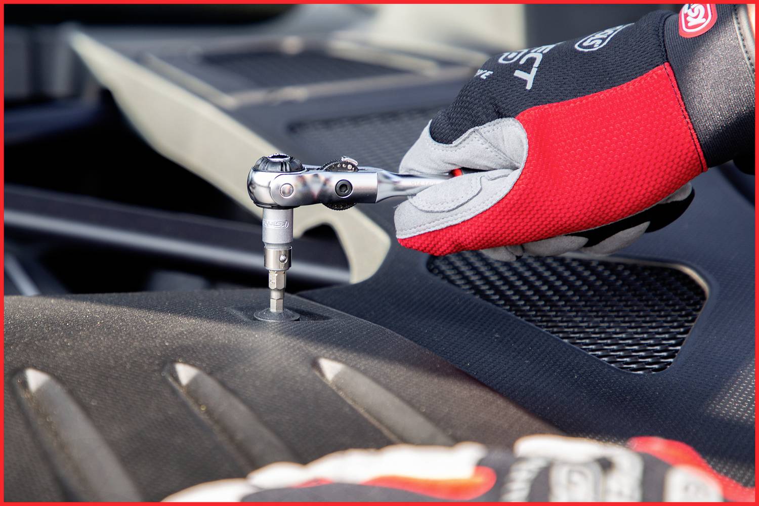 Eine Person mit roten Handschuhen benutzt einen Steckschlüsselschlüssel, um an einem Motorblock zu arbeiten.