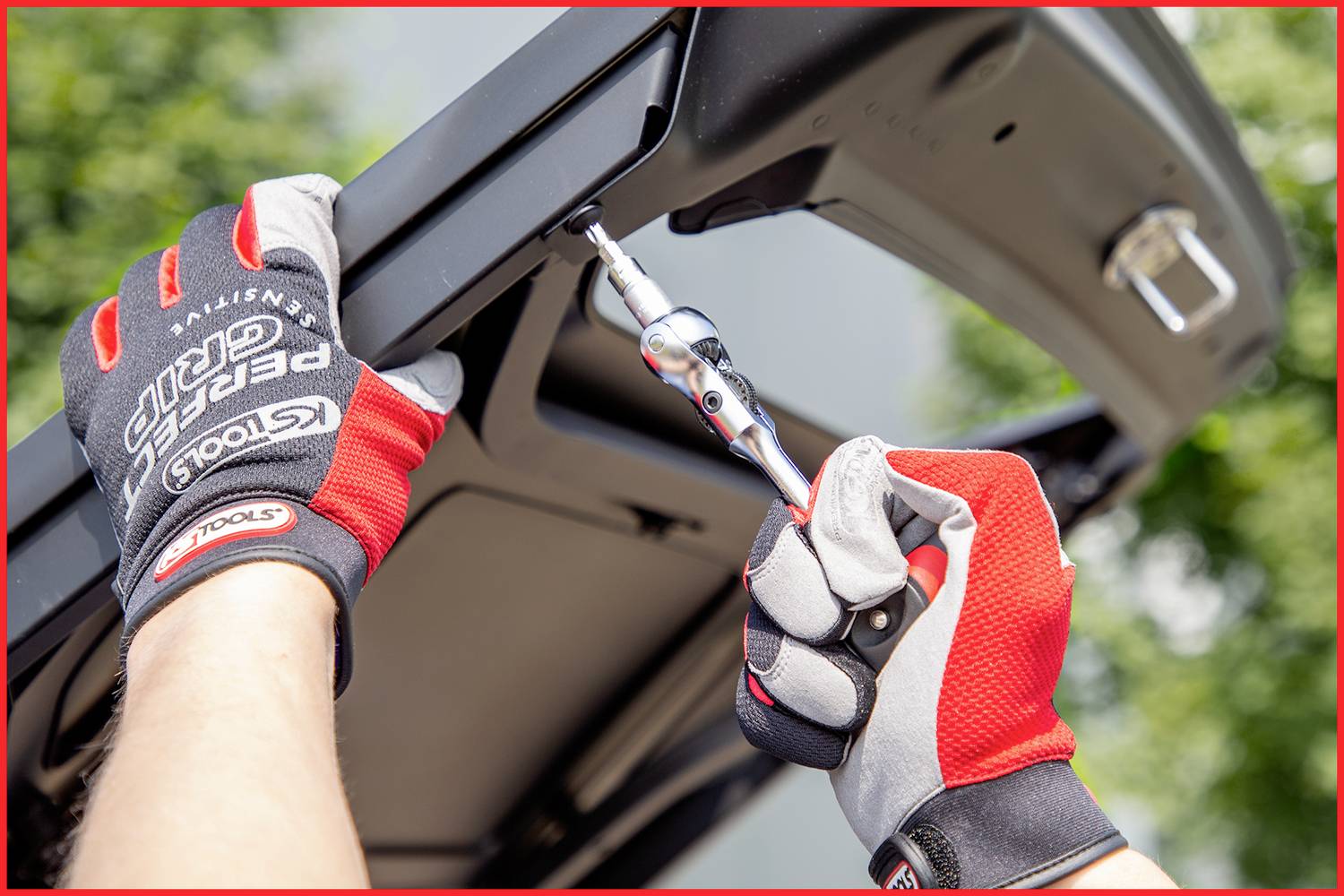 Eine Person mit Handschuhen verwendet einen Schraubenschlüssel, um eine Schraube am Autoheck zu ziehen.