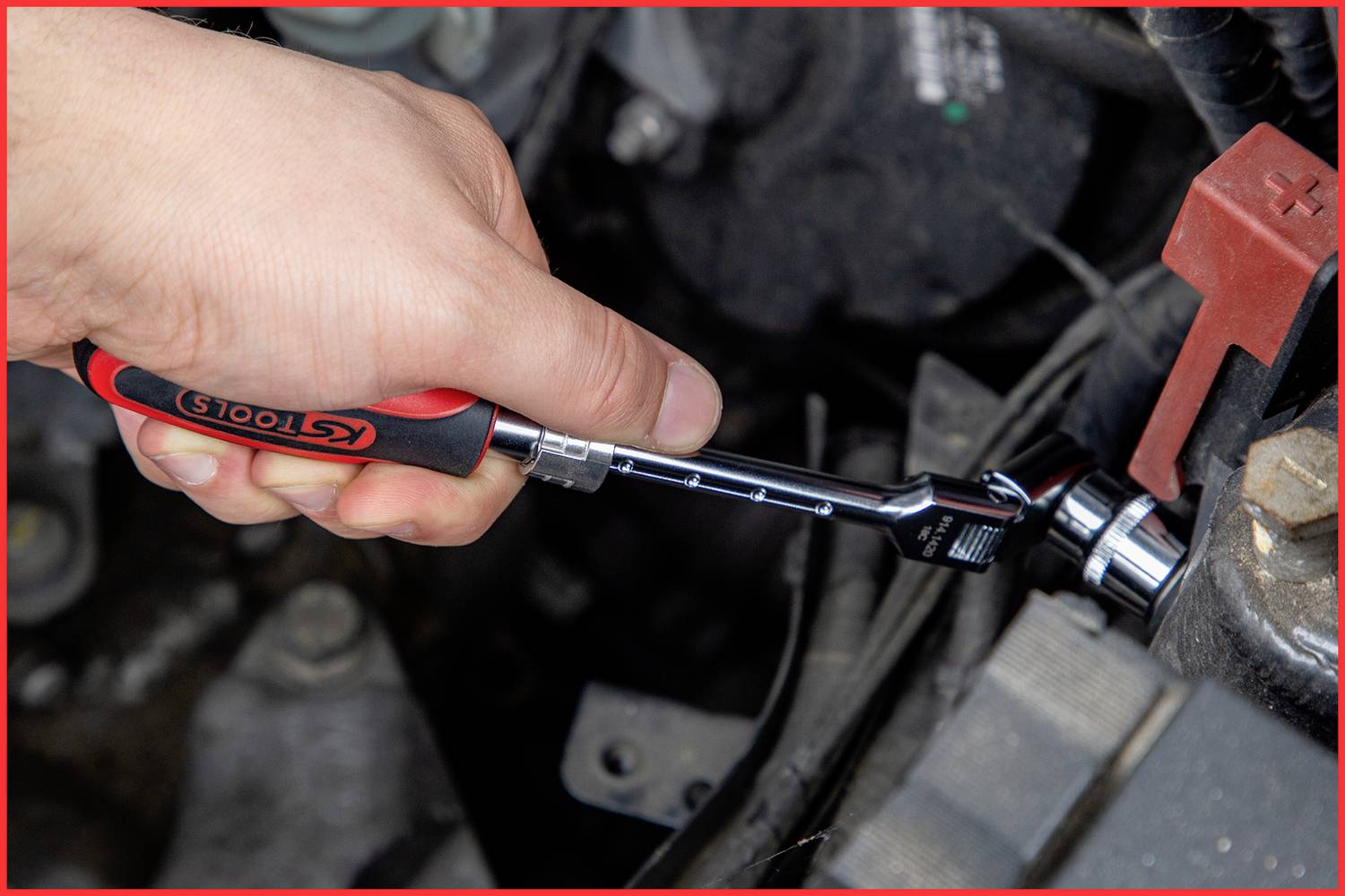 Eine Hand benutzt einen Ratschen-Schlüssel, um eine Mutter in einem Motorraum zu befestigen. Der Schlüssel trägt das Logo 'KS TOOLS'.