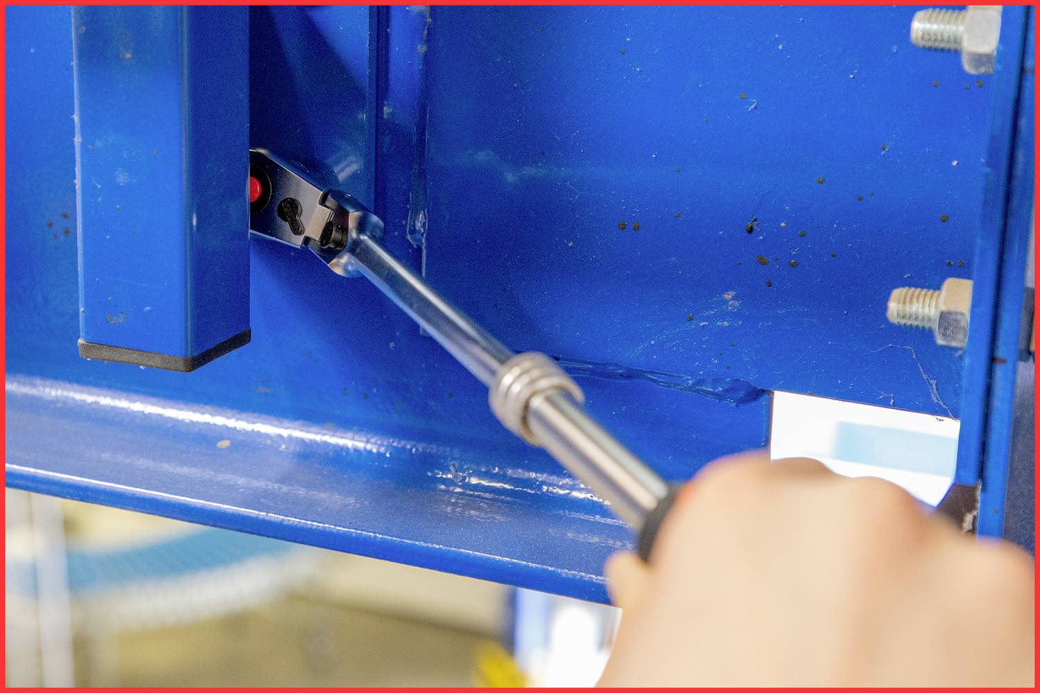 Eine Hand spannt mit einem Schraubendreher eine Schraube in einer blauen Metallkonstruktion an.