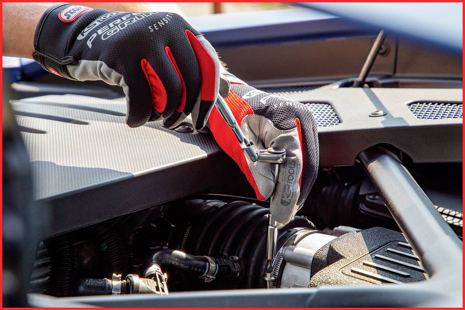 Eine Person in Arbeitshandschuhen zieht mit einem Schraubenschlüssel eine Schraube am Motor eines Autos fest.