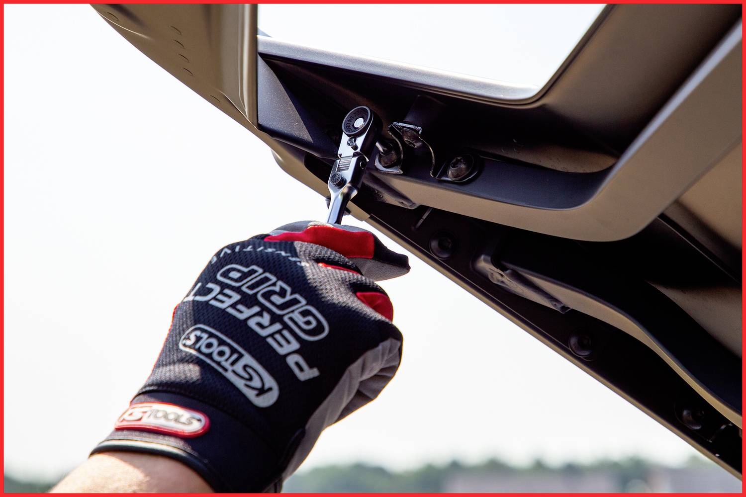 Eine Person repariert mit einem Schraubendreher ein Teil am Fahrzeugdach, während sie einen Handschuh trägt.