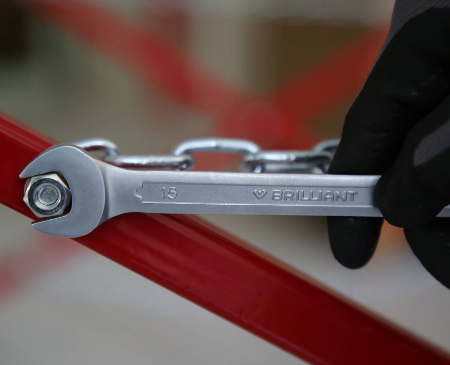 Eine Hand mit Handschuh hält einen Schraubenschlüssel, der eine Mutter an einer roten Metallstruktur festzieht.