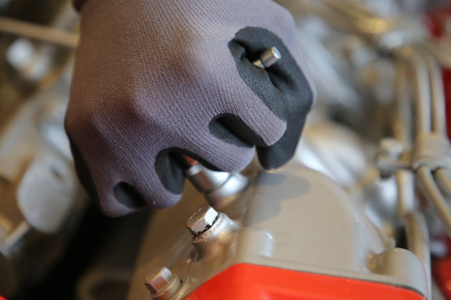 Eine Hand mit Arbeitshandschuh zieht eine Schraube an einem technischen Gerät an, Fokus auf die Handbewegung und Schraube.