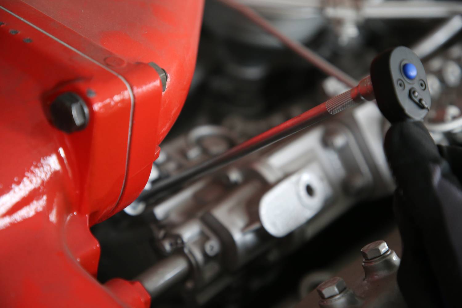 Roter Motorblock und Metallteile eines Automotors, teilweise verdeckt durch eine Hand mit einem Schraubenschlüssel.