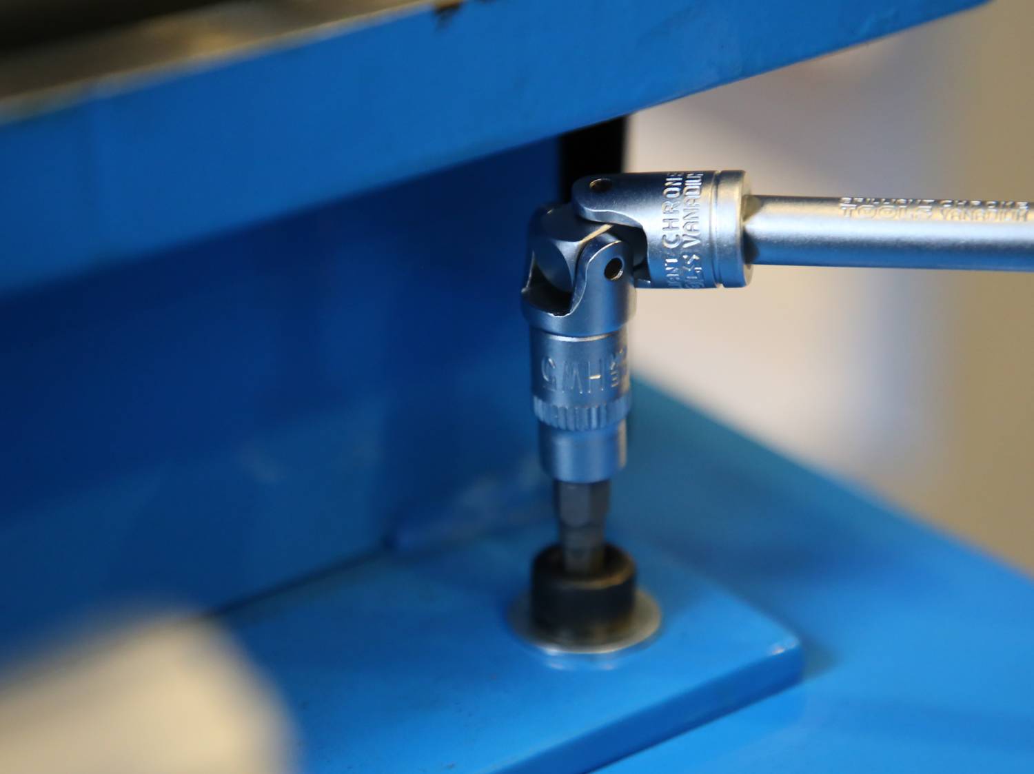 Ein Steckschlüssel wird auf eine Schraube angesetzt, um sie zu befestigen. Die Szene zeigt einen blauen Hintergrund mit einem Metallaufsatz.