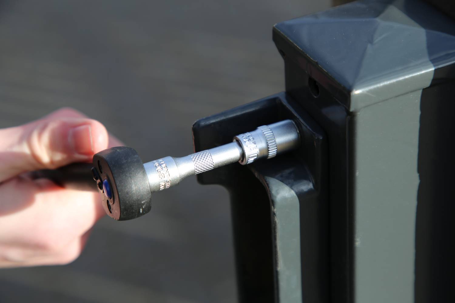 Eine Hand benutzt ein Drehmomentschlüssel, um eine Schraube an einem Metallzaun festzuziehen.