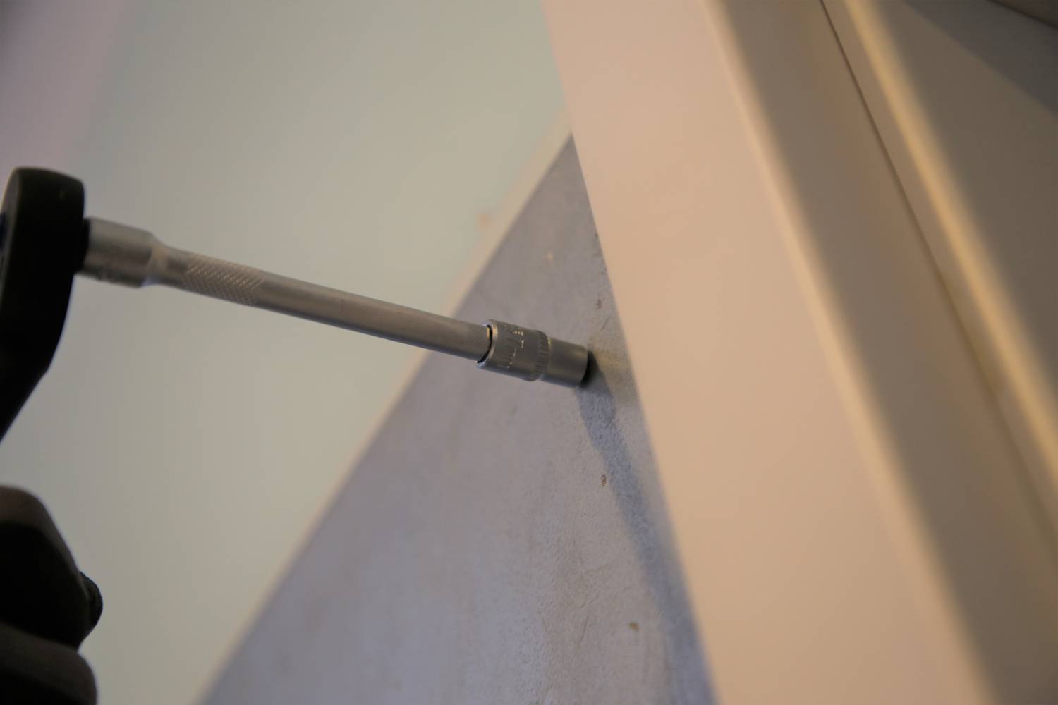 Eine Schraube wird mit einem Schraubendreher in eine graue Oberfläche eingeschraubt, möglicherweise während eines Montageprozesses.