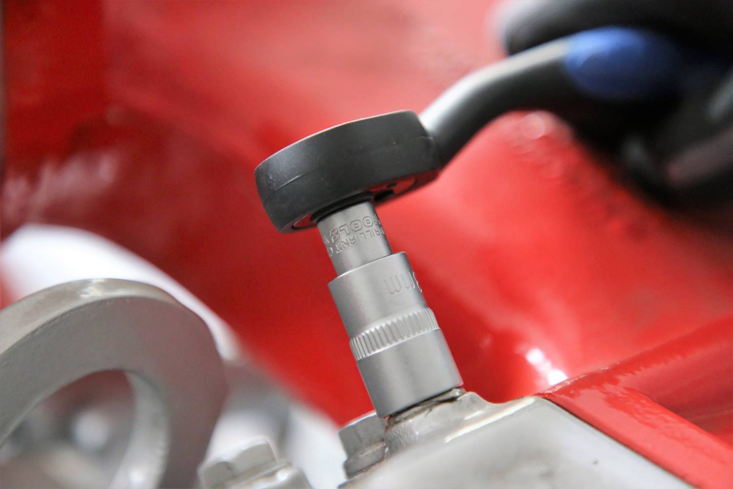 Nahaufnahme eines Spannschlüssels, der eine Schraube an einer roten Maschinenkomponente anzieht. Eine Hand hält den Schlüssel fest.