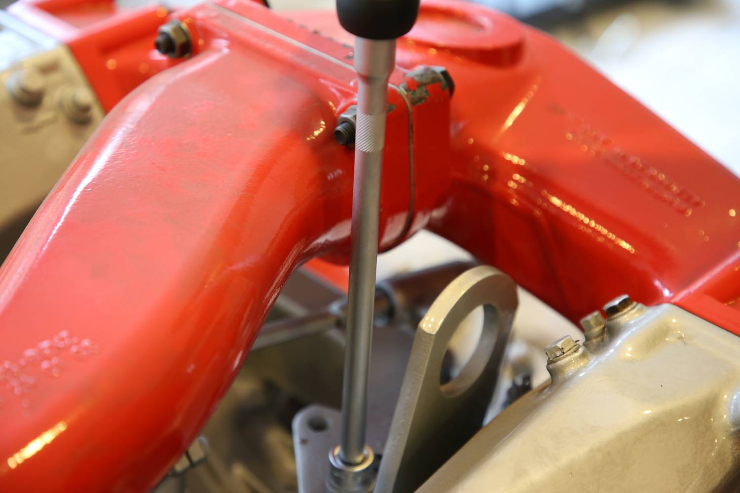 Rotes mechanisches Teil mit Hebel, vermutlich Teil eines Motors oder Maschinenbauteils. Fokus auf Hebel und Befestigungen.