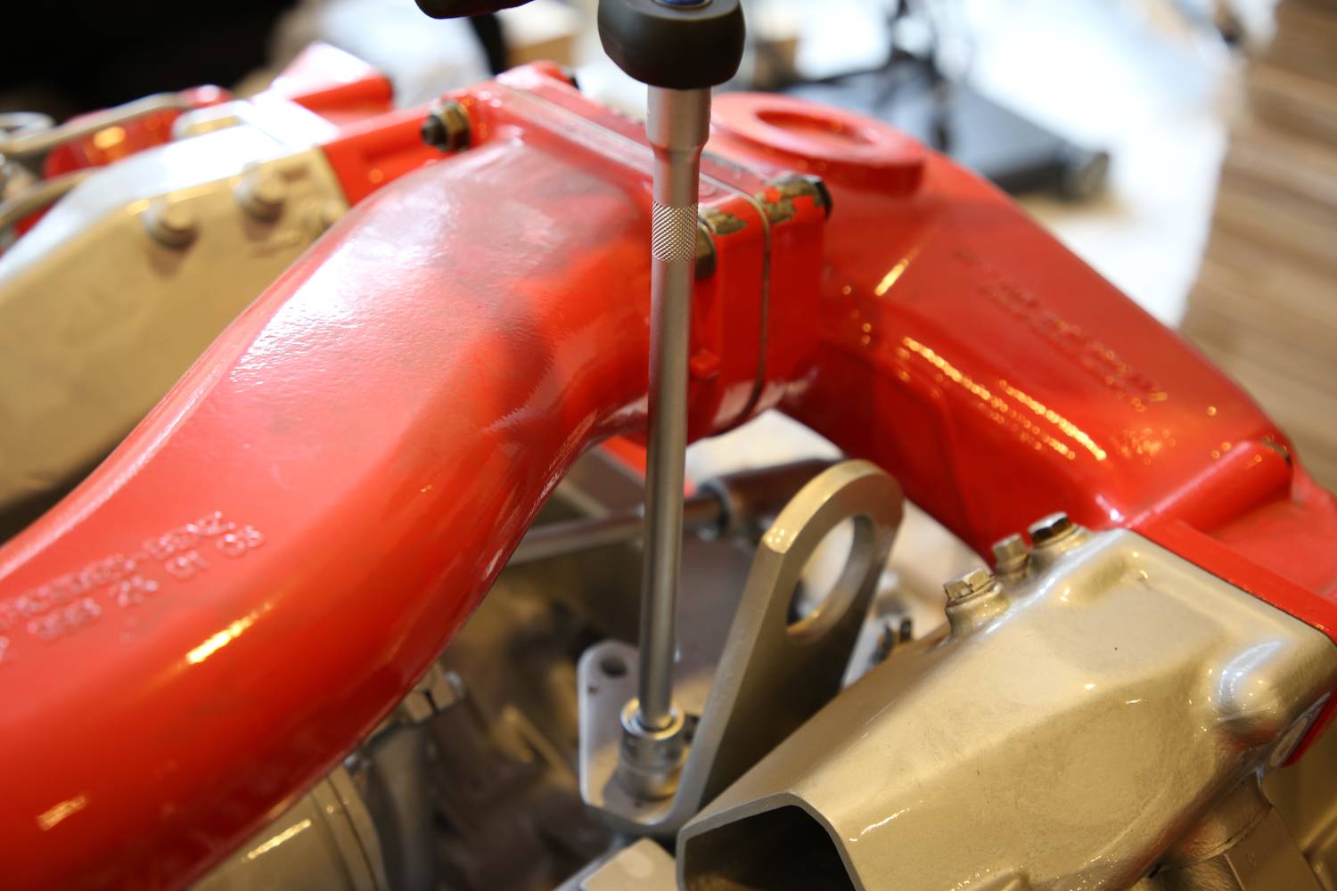 Mechanischer Schraubendreher zieht Schraube an rotem Metallrohr fest, das mit Motorbauteilen verbunden ist. Nahe Aufnahme der Mechanik.