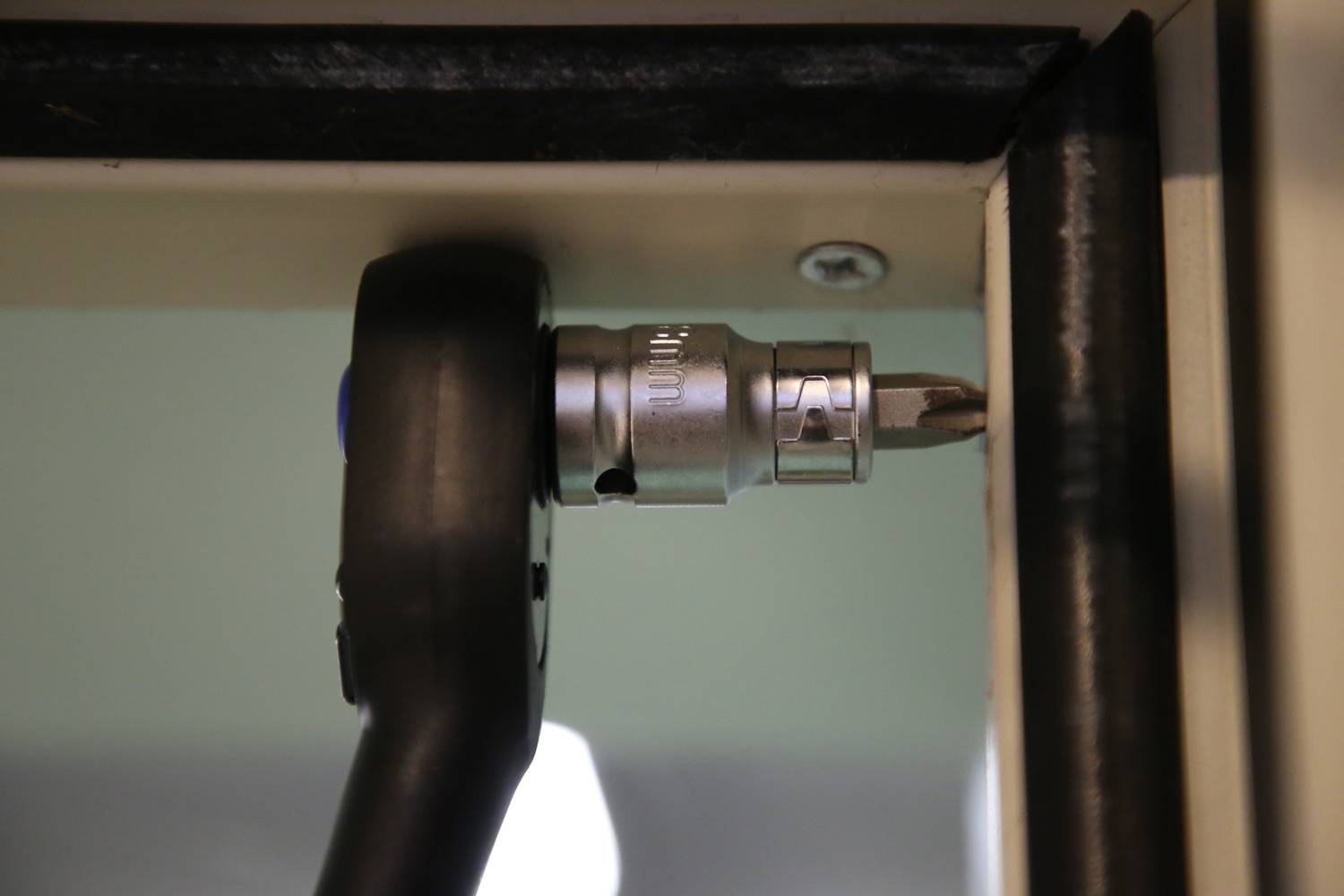 Ein Ratschenwerkzeug zieht eine Schraube in eine Metallkante ein. Es zeigt mechanische Arbeit an einer Konstruktion oder einem Gerät.