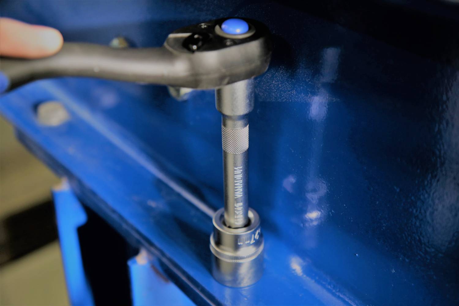 Ein Handwerker benutzt eine Ratsche zum Festziehen einer blauen Metallkomponente. Die Ratsche hat einen blauen Knopf oben.