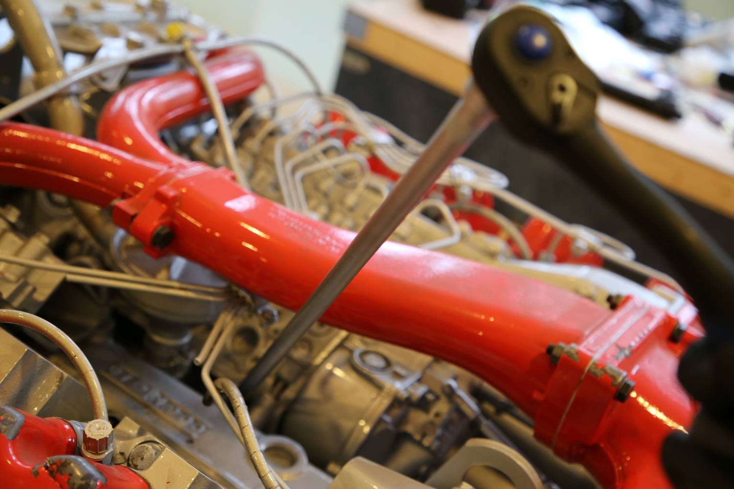 Roter Motor im Fokus, möglicherweise Schiffsmotor, mit Werkzeug und Schrauben. Werkstatt im Hintergrund. Thema: Mechanik/Instandhaltung.