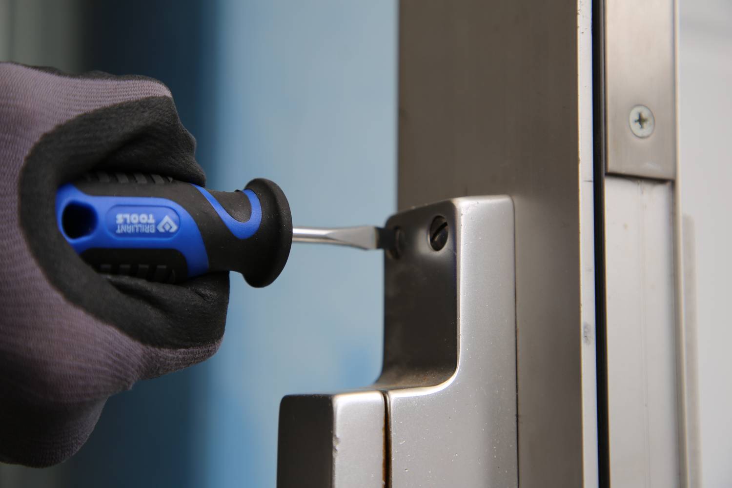 Person mit Handschuh benutzt Schraubendreher, um Türschloss zu manipulieren.