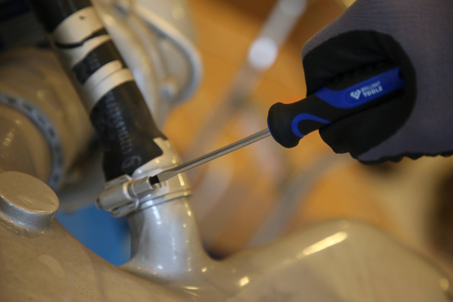Eine Person zieht mit einem Schraubendreher eine Schlauchschelle fest, vermutlich an einem Rohr.