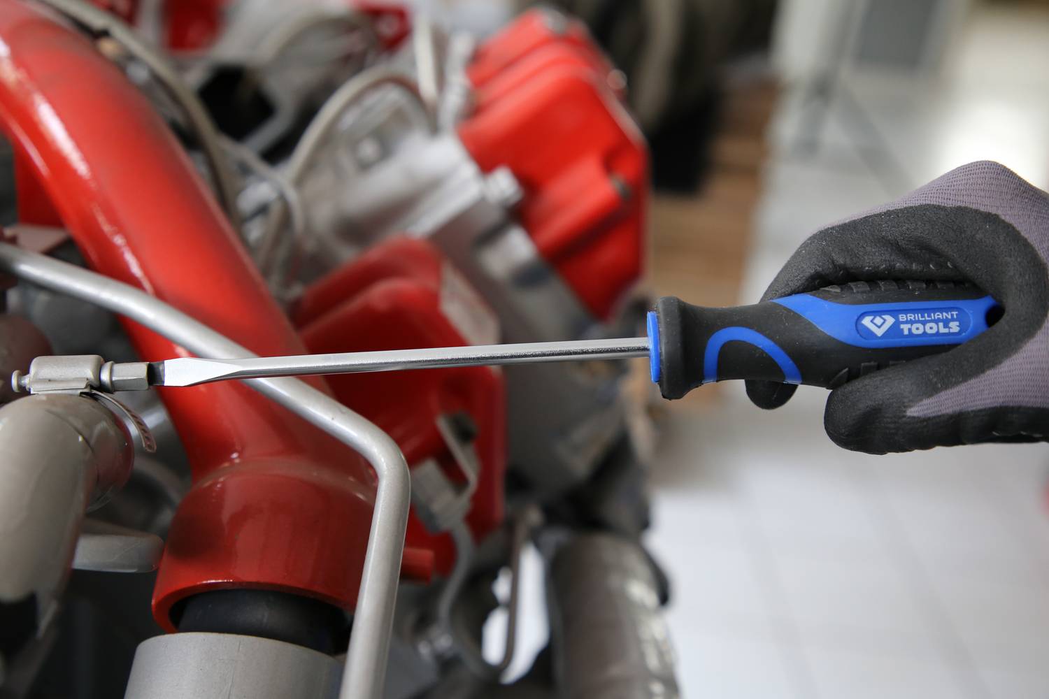 Eine Person zieht mit einem Schraubendreher eine Schraube an einem roten Gerät an. Im Hintergrund unscharf weitere Werkzeuge.