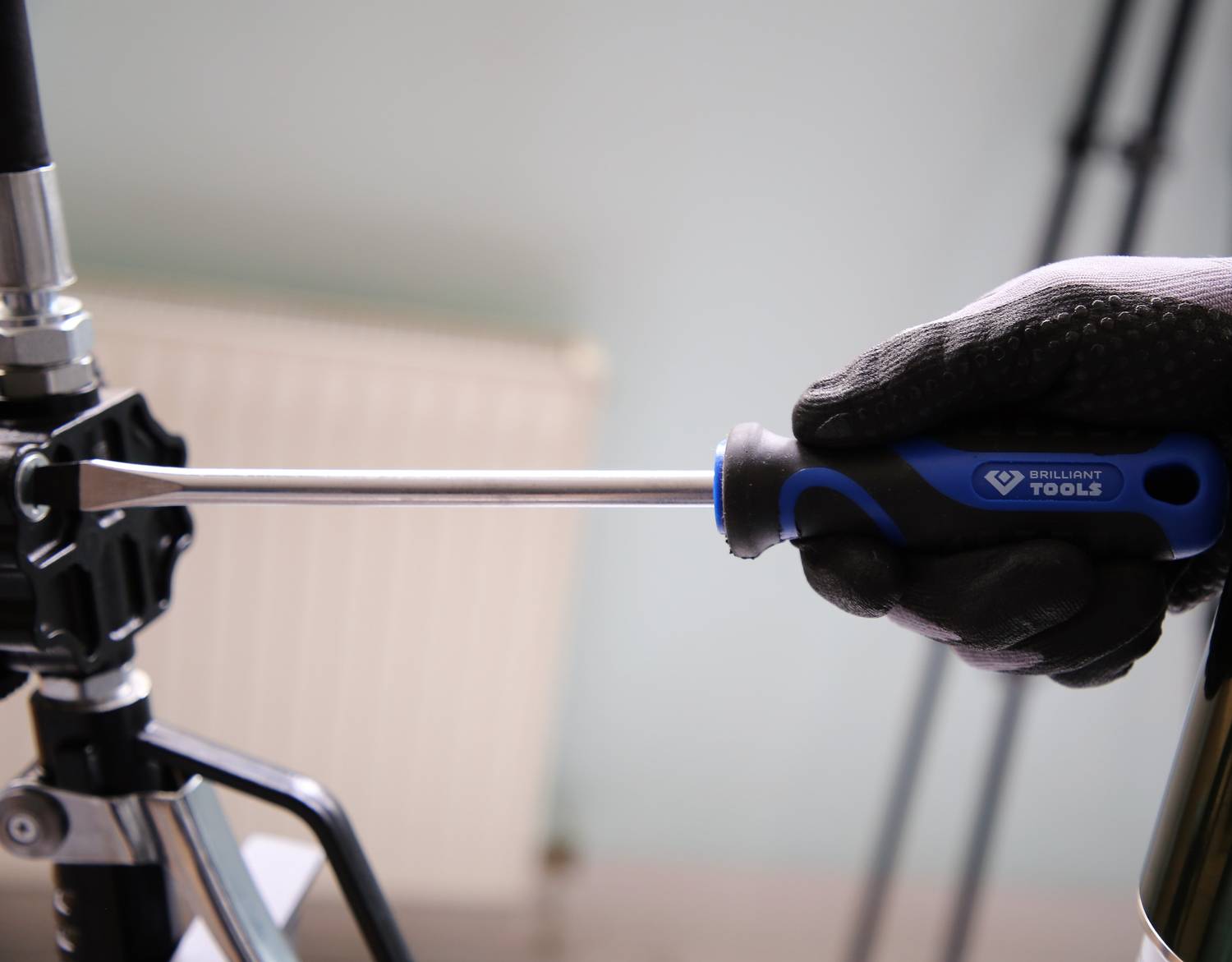 Eine behandschuhte Hand benutzt einen Schraubenzieher, um eine Schraube an einem metallischen Gerät zu drehen.