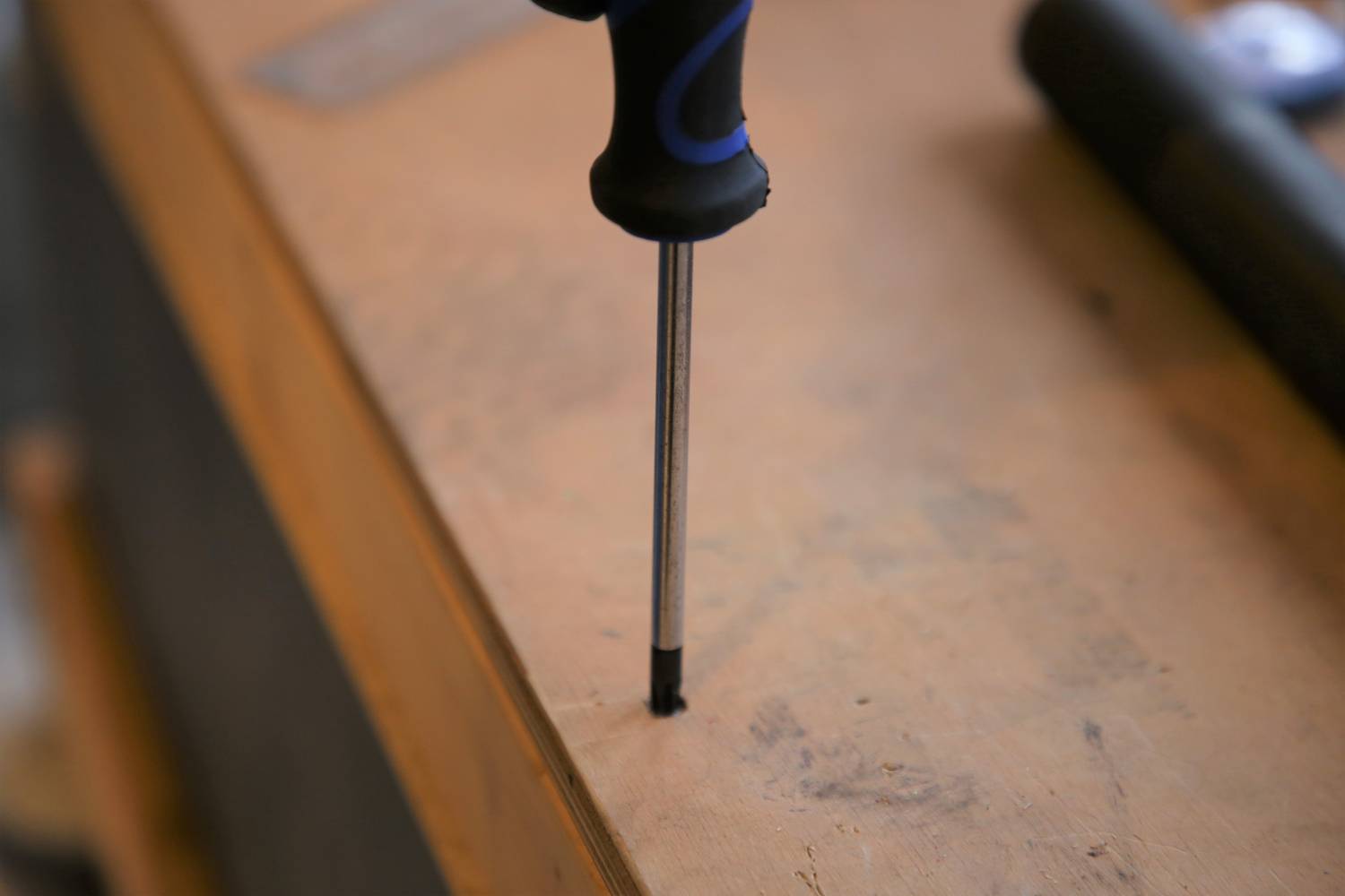 Ein Schraubendreher steht aufrecht auf einer Holzoberfläche, der Handgriff zeigt nach oben.