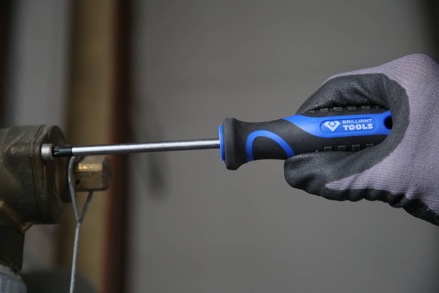 Eine Hand mit Handschuh hält einen blauen Schraubendreher und zieht eine Schraube in eine Metallhalterung fest.