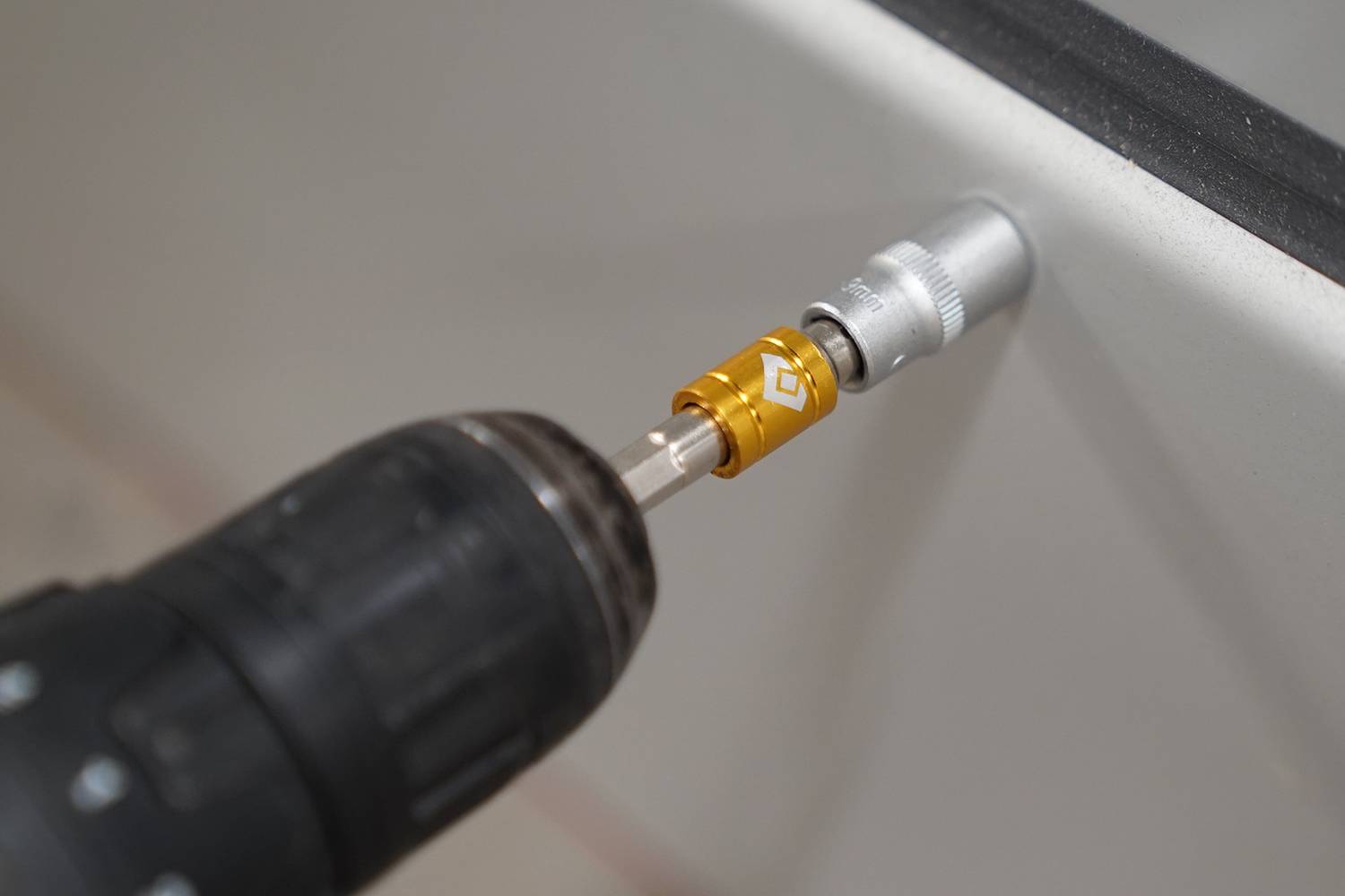 Eine Bohrmaschine zieht eine Schraube in eine weiße Oberfläche ein. Die Schraubenkopfaufnahme des Bohrers ist golden.
