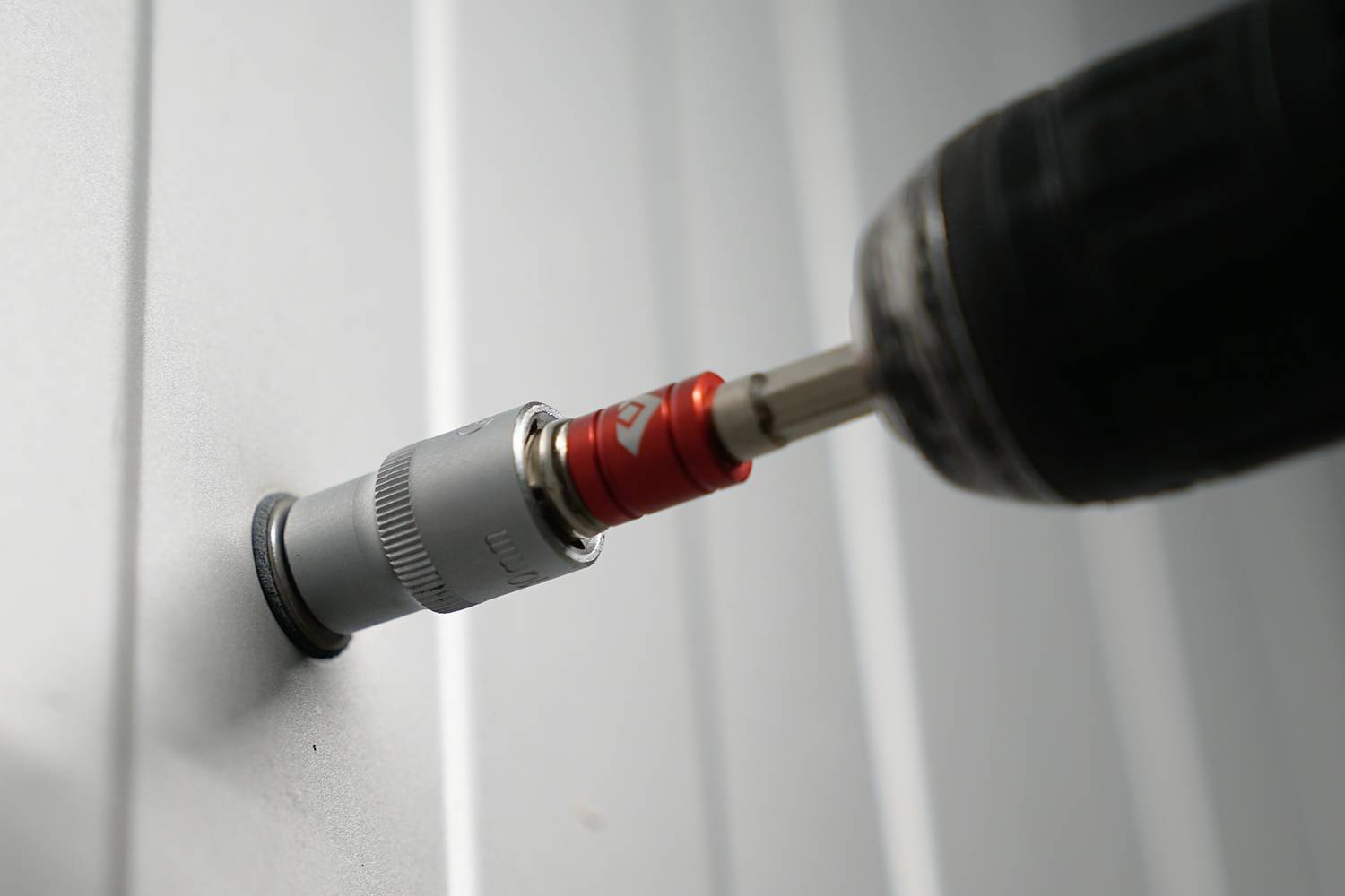 Ein Akkuschrauber zieht eine Schraube in eine Metallwand, zeigt Nutzung von Elektrowerkzeugen bei Bau- oder Montagearbeiten.