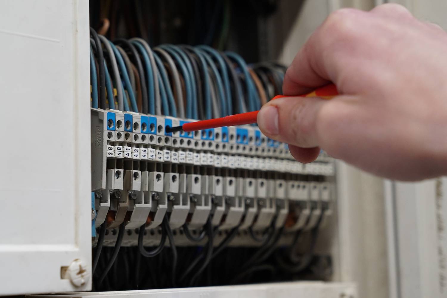 Hand mit Schraubenzieher repariert einen elektrischen Schaltschrank mit vielen Kabeln und Anschlussklemmen.