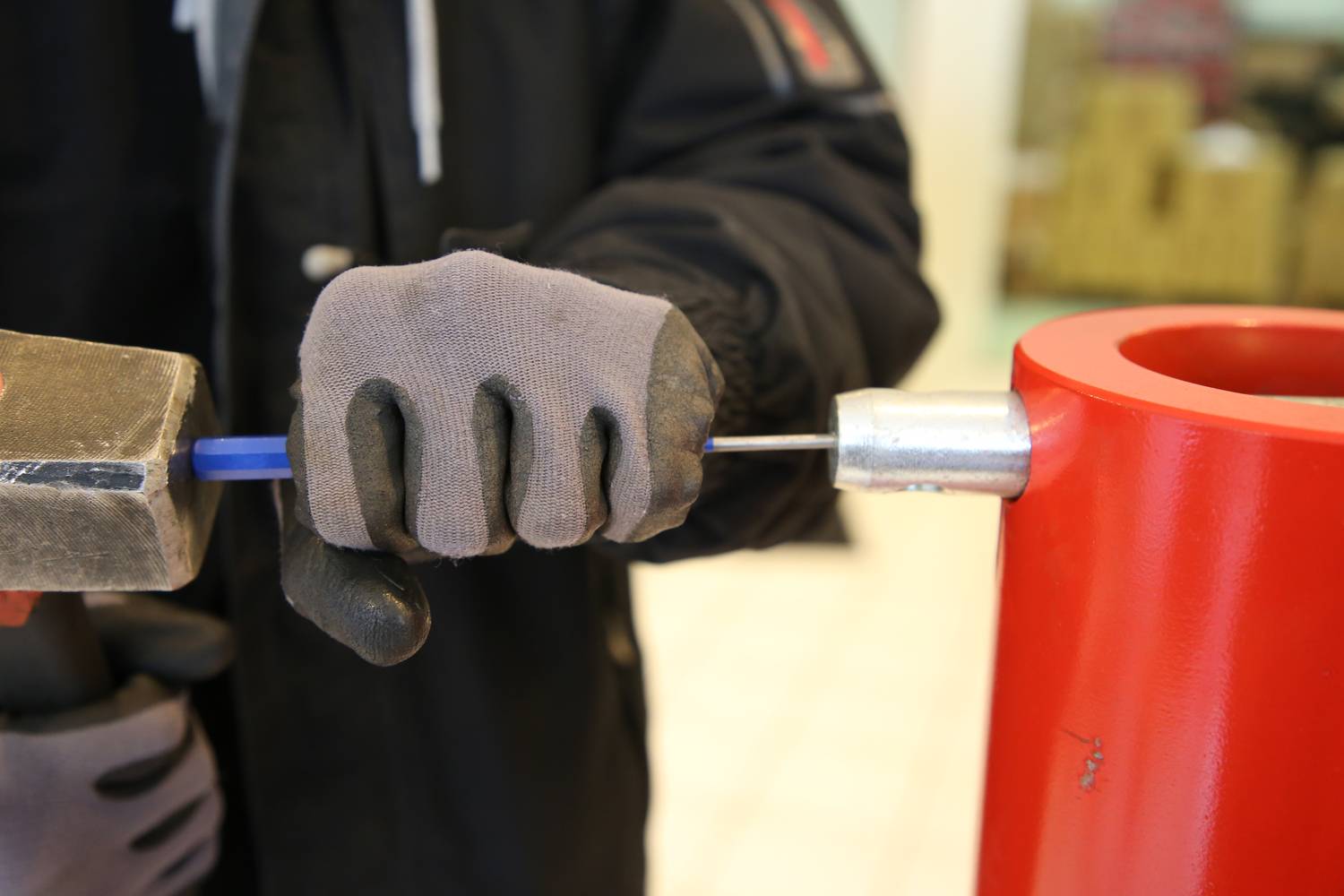 Eine Person befestigt mit einem Hammer ein Metallelement an einem blauen Stab, der in einem roten Metallteil steckt.
