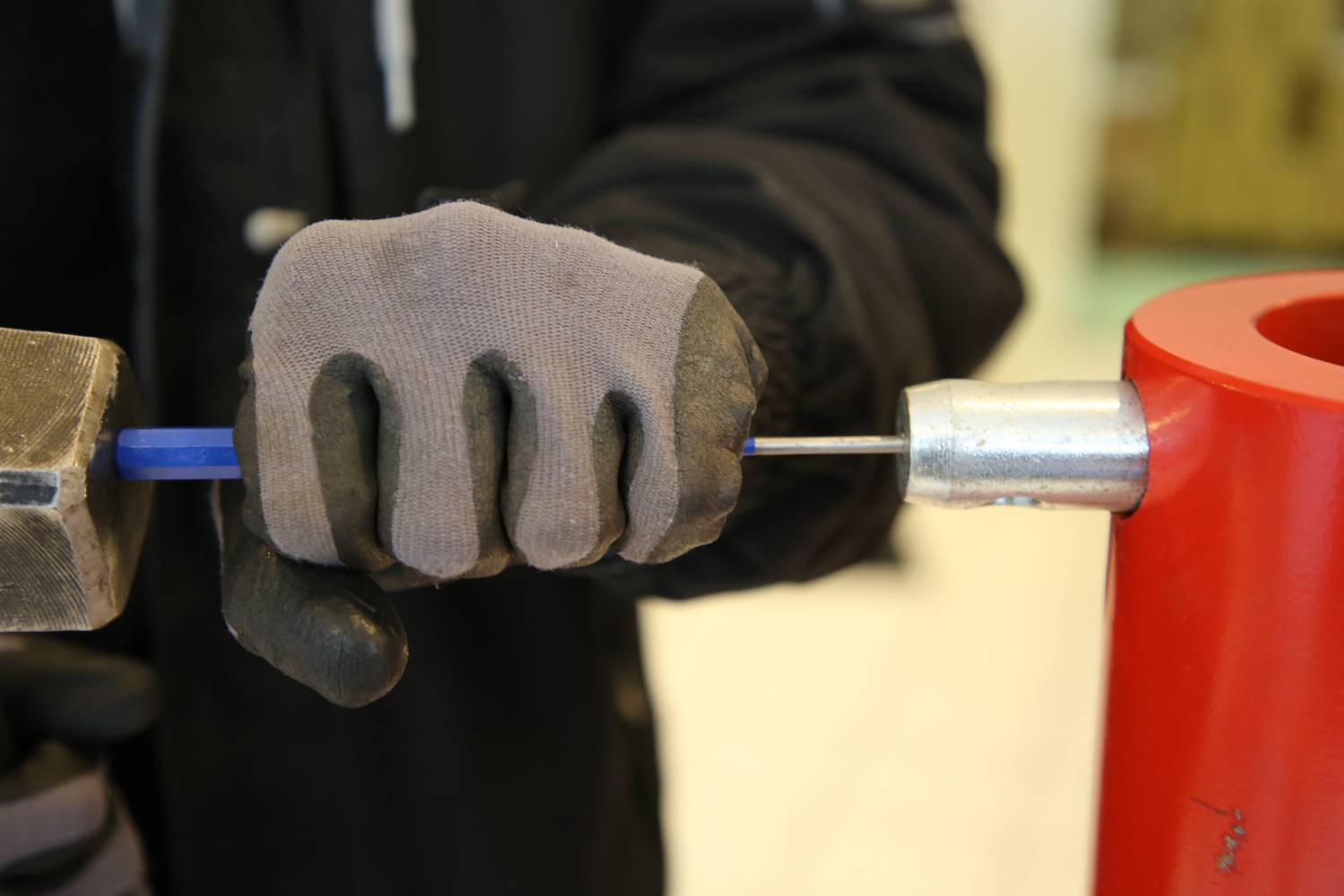 Eine Person in Arbeitshandschuhen spannt mit einem Werkzeug einen dünnen blauen Draht in ein rotes Gerät ein.
