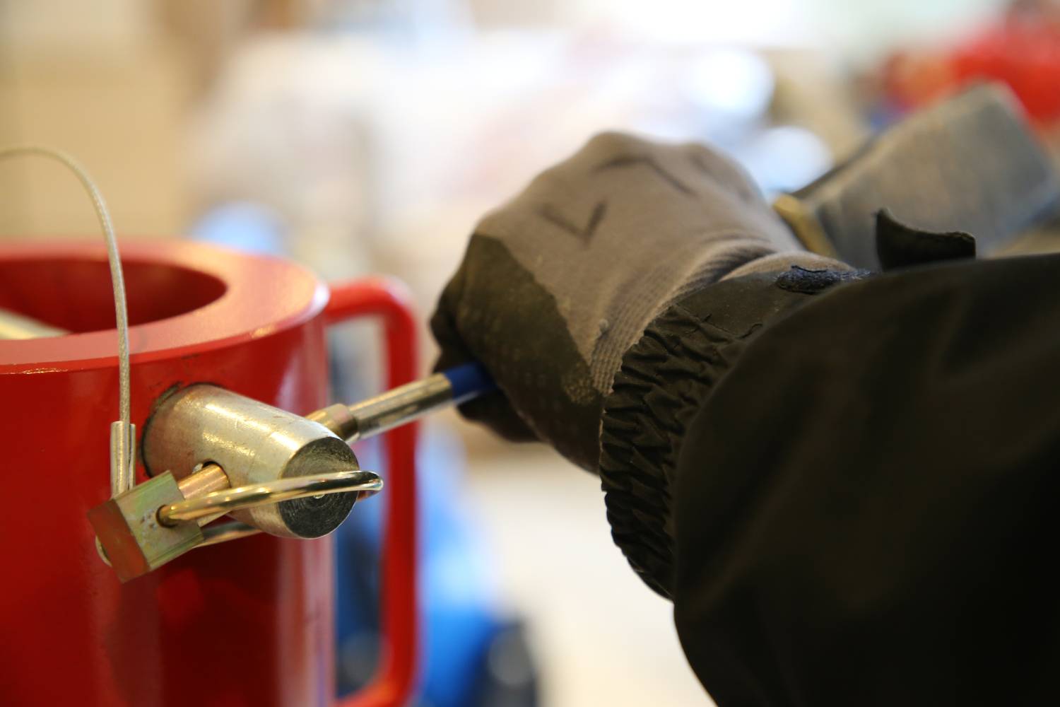 Eine Person mit Handschuhen arbeitet mit einem blauen Gerät an einem roten Behälter, möglicherweise bei einer technischen Wartung.