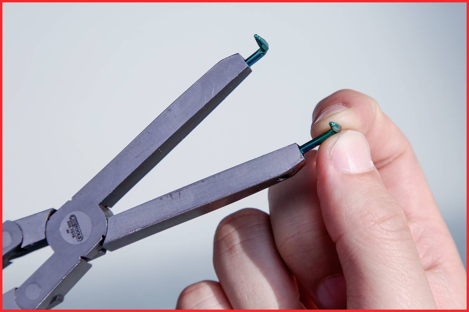 Eine Hand entfernt mit einer Zange ein Piercing aus einem Ohrläppchen.