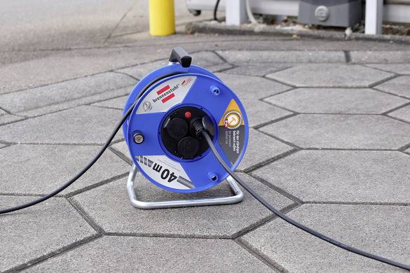 Eine blaue Kabeltrommel für 40 Meter Kabel liegt auf einer gepflasterten Fläche. Ein Kabel ist herausgezogen und angeschlossen.