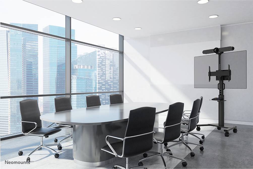 Konferenzraum mit großem Tisch und acht Stühlen, Blick auf moderne Hochhäuser durch große Fenster. Ein Bildschirm steht bereit.