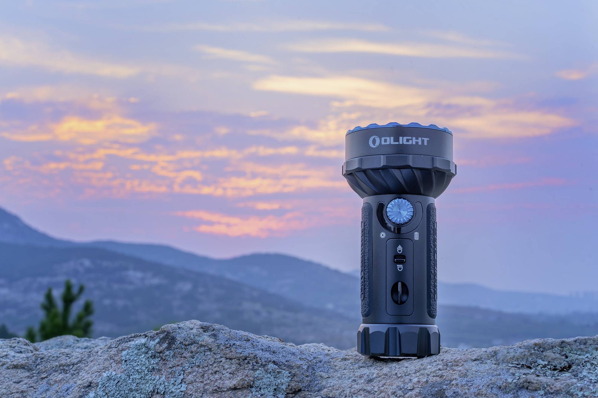 Eine Taschenlampe steht auf einem Felsen, im Hintergrund ein farbenfroher Sonnenuntergang über einer hügeligen Landschaft.