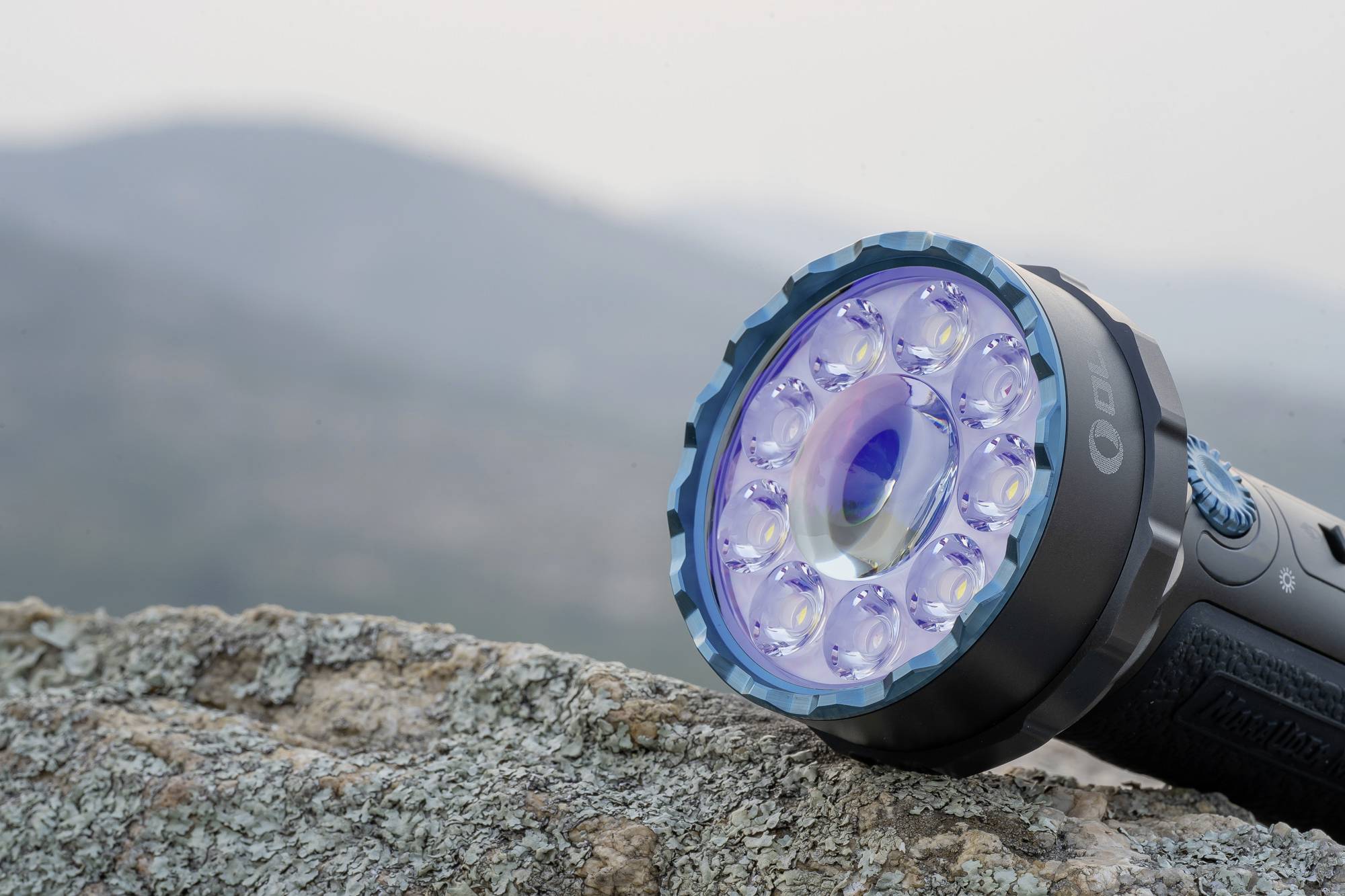 Taschenlampe leuchtet mit LED-Lichtern auf einem Felsen; unscharfer Hintergrund zeigt Berge und klaren Himmel.