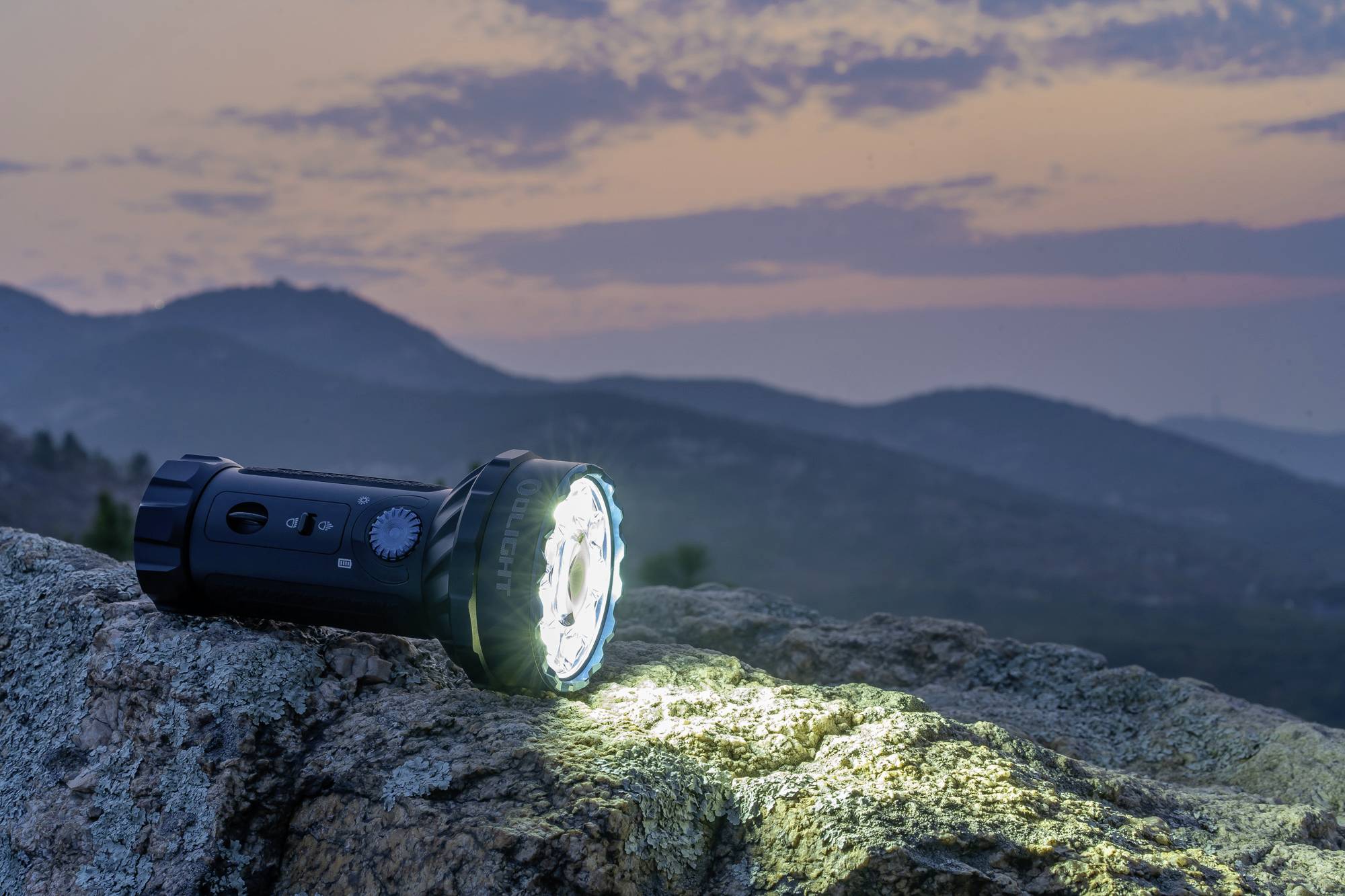 Taschenlampe leuchtet auf einem Felsen in der Dämmerung, mit Hügeln und einem pastellfarbenen Himmel im Hintergrund.