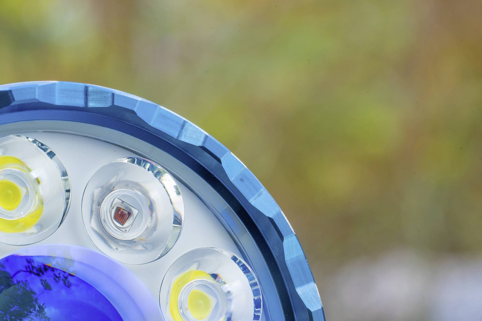 Nahaufnahme einer LED-Taschenlampe, zeigt die Leuchten unter einem blauen Rand. Hintergrund ist unscharf und herbstlich.