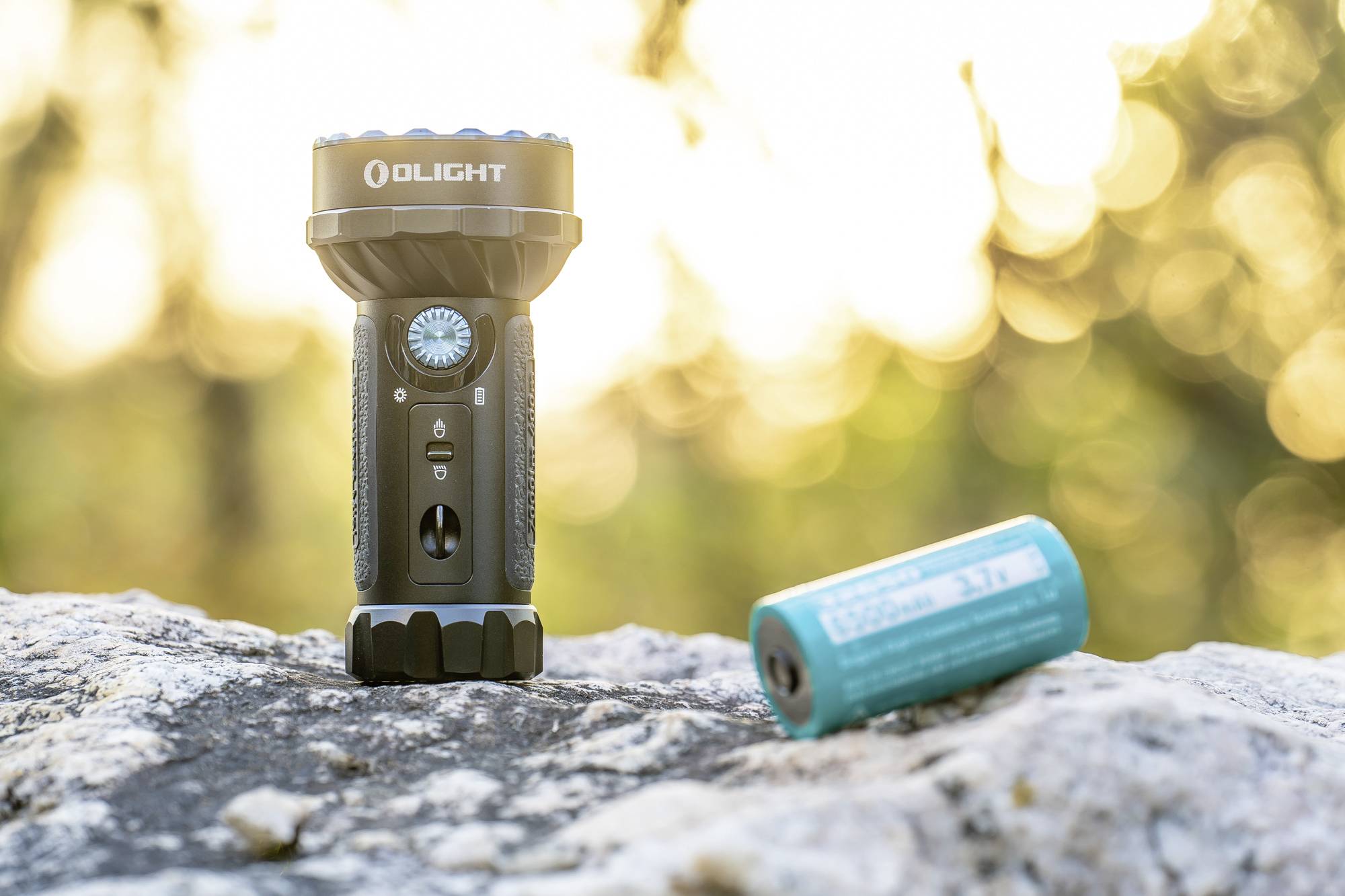 Eine schwarze Taschenlampe mit silbernem Kopf steht auf einem Felsen neben einer blauen Batterie vor einem verschwommenen Hintergrund.
