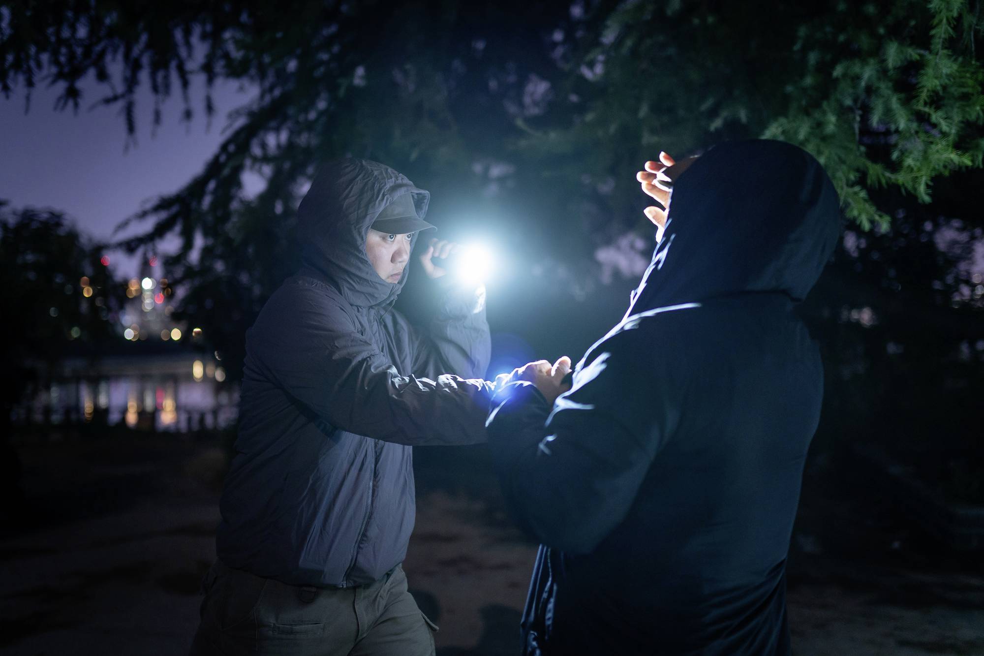 Zwei Personen in Winterkleidung stehen draußen im Dunkeln. Eine Person leuchtet der anderen mit einer Taschenlampe ins Gesicht.