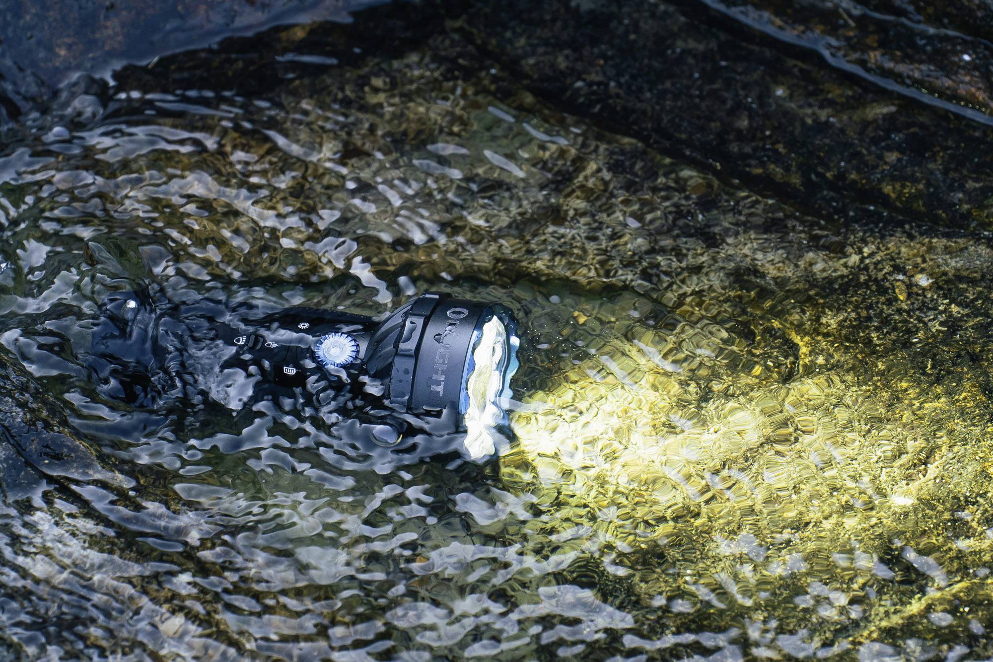 Taschenlampe leuchtet unter Wasser auf steinigem Flussbett, zeigt Wasserdichtigkeit und robustes Design bei nassen Bedingungen.